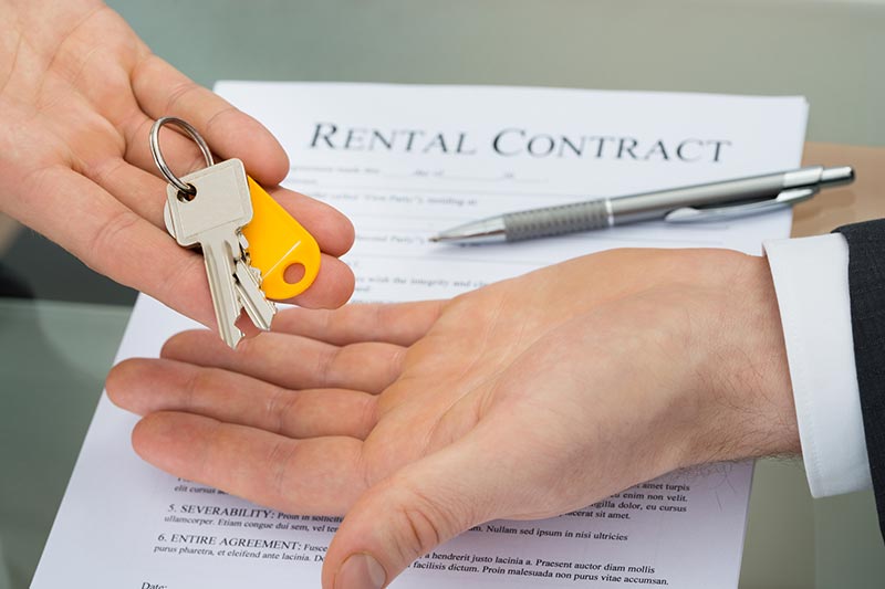 Person giving keys to another person with a rental contract below them.